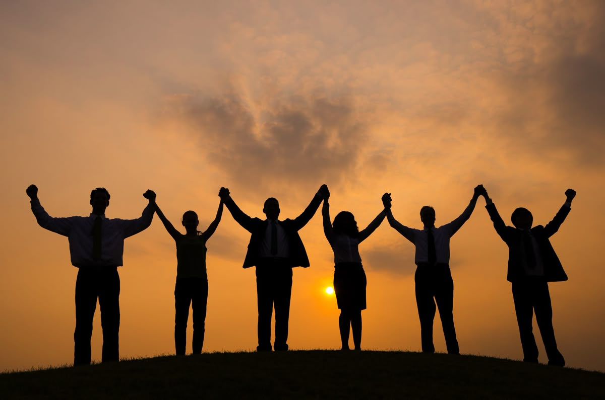 Members standing together with raised, joined hands at sunset